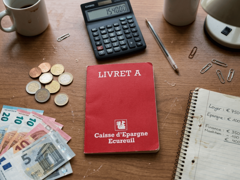 Livret A posé sur un bureau près d'une calculatrice, quelques billets en euro et quelques pièces